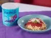 Fotografia de um prato fundo azul, pequeno, sobre um pano roxo, ao lado de uma lata de Ascenda. Dentro do prato tem macarrão tradicional com o molho de tomate e ascenda.