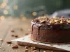 Fotografia de um bolo de chocolate decorado com ganache brilhante e nozes, apresentado em uma superfície de madeira. O fundo desfocado com luzes quentes cria uma atmosfera acolhedora, ideal para celebrações.