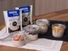 Receita de overnight oats proteico para a semana servida em potes herméticos de vidro sobre uma mesa de madeira decorada com panos e embalagens de aveia proteína