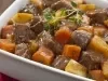 Fotografia em tons de marrom com um paninho vermelho e um recipiente branco retangular com picadinho de carne com batatas e cenoura