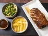 Pernil suíno assado com mandioca dourada, salada de folhas com laranja e molho servido à parte, apresentado em travessas.
