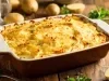 Em cima de uma mesa, refratário retangular com batatas e queijo gratinado, decoado com cheiro-verde picado.