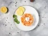 Fotografia vista de cima em tons claros de uma mesa de cimento queimado claro. Sobre a mesa tem um prato branco raso com tartar de salmão sobre abacate em cubos ao lado de duas rodelas de limão siciliano.