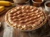 Em cima de uma mesa, banoffe em refratário, decorado com chantilly e canela em pó.