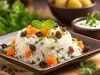 Em um prato de porcelana marrom, há uma porção de arroz branco misturado com cenouras, ervilhas e uvas-passas, decorado com duas folhas de hortelã.