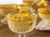 Fotografia apresenta uma mousse de maracujá servida em uma taça elegante. A mousse tem uma textura leve e cremosa, decorada com sementes de maracujá frescas e uma calda amarela