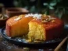 Fotografia de um bolo de semolina, com crosta dourada e interior macio. Decorado com pistachios e flocos de coco, em um prato escuro.