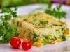 Imagem de frente de um prato de porcelana branco com uma porção colorida de arroz amarelo, milho verde,  ervilha, decorados com dois tomates-cerejas e galhos de coentro.
