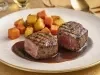 Dois bifes altos ao ponto servidos com molho reduzido escuro e raízes assadas douradas, apresentados em prato branco elegante