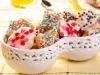 Em cima de uma mesa, tigelas com biscoitos redondos e em formato de coração com glacê branco e confeitos coloridos.