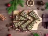 Em cima de uma mesa, tábua com brownie em forma de triângulo, decorado com creme verde e confeitos de bolinhas e estrelas.