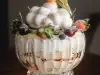 Foto aproximada da receita de Pavlova na taça, montada em uma linda taça de cristal com camadas de creme, merengue e frutas amarelas e vermelhas. Decorada com um lindo merengue no topo.