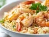 Prato branco com porção de arroz cremoso e camarão, decorado com uma folha de coentro.