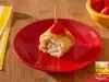 Enroladinho de omelete recheado com creme de Ninho, sobre prato vermelho, finalizado com tomate cereja e palito.