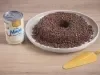 Foto da receita de Brigadeirão Moça, servido em um prato branco, decorado com muitos granulados de chocolate. O prato está entre uma lata de Leite Moça e uma espátula dourada, tudo sobre uma bancada de madeira