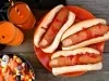 Cachorro-quente com salsichas em formato de dedo, pão macio e dourado, corte superficial na ponta simulando unha, com ketchup vermelho escorrendo.