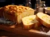 Fotografia de um bolo de queijo recém-assado, com crosta dourada e queijo derretido, exibido em uma tábua de madeira. O interior é macio e fofo, sugerindo um ambiente acolhedor e caseiro.