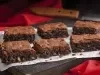 Foto de 6 pedaços iguais de brownie em cima de uma toalha branca e com uma faca de serra ao fundo da foto
