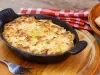 Em cima de uma mesa, refratário preto com queijo gratinado.