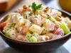 Em cima de uma mesa,  tigela com salada de maionese com cenouras, batatas e salsão, decoradas com nozes picadas e folha de cheiro-verde.