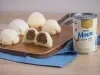 Receita de Mochi de Brigadeiro, servida em pequenas bolinhas brancas, recheadas com brigadeiro enrolado, sobre uma tábua de madeira e um tecido na cor azul ao lado de uma Lata de Leite Moça