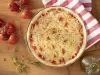 Imagem vista de cima de uma pizza redonda de queijo muçarela. Ao lado, um paninho listrado branco e vermelho e tomates.