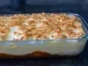 Imagem de uma travessa de vidro com a sobremesa chico balanceado. É possível ver a camada de caramelo com banana, creme branco e merengue dourado.