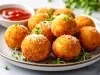 Em cima de uma mesa, prato cinza com porção de bolinho dourado e crocante, polvilhado com queijo ralado.
