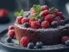 Fotografia de um bolo de chocolate elegantemente apresentado, coberto com framboesas frescas e polvilhado com açúcar de confeiteiro, em um prato escuro. O fundo desfocado destaca a sofisticação.