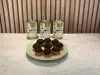 Prato verde-claro com brigadeiros cobertos com granulado de chocolate e latas de Leite Moça ao fundo.