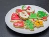 Em cima de uma mesa, prato branco com biscoitos de papai Noel, árvore de Natal e botas, decorados com glacê colorido e confeitos de bolinha coloridos.
