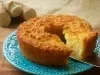 Imagem de um prato azul com detalhes e o bolo de aipim com uma fatia na espátula. Ao fundo, mandiocas.