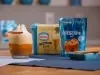 Copo com bebida cremosa ao lado de um sachê azul de NESCAFÉ® Ice e um prato com canela em pau.