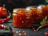 Imagem de três potes de geleia de pimenta e ao lado, pimentas vermelhas.
