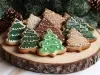 Em cima de uma mesa, prato de madeira com biscoitos em formato de Árvore de Natal, decorados com glacê colorido, chocolate derretido e confeito colorido.