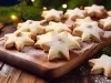 Em cima de uma mesa, prato com biscoitos em formato de estrelas, polvilhados com açúcar de confeiteiro.