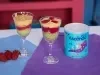 Fotografia em tons claros de duas taças de vidro com os cremes coloridos intercalados com o biscoito nesfit. As taças estão sobre dois panis, azul e roxo, ao lado tem a lata de ascenda e três morangos inteiros.