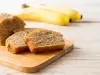 Imagem de fatias de um bolo retangular de banana sobre uma tábua de madeira e ao fundo duas bananas.