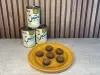 Seis brigadeiros caramelizados em forminhas azuis sobre prato amarelo, com três latas de LEITE MOÇA® ao fundo.
