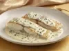 Filé de peixe branco dourado servido no molho cremoso de ervas, apresentado em prato fundo branco com acabamento sofisticado.