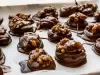 Em cima de uma mesa com papel-manteiga, bolinhas com chocolate derretido, decorado com nozes.