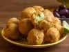 Em cima de uma mesa, prato amarelo com porção de bolinhos de bacalhau dourados e crocantes. No lado direito, há um bolinho aberto ao meio com bacalhau cremoso.
