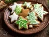 Em cima de uma mesa, prato redondo com porção de biscoitos em forma de estrela, decorados com glacê branco e verde.