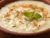 Tigela redonda de porcelana marrom com arroz cremoso com canela em pó, decorado com alecrim e folha de hortelã.