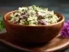 Fotografia de uma salada colorida em uma tigela de madeira, com repolho verde e roxo, ervas frescas e um molho cremoso.