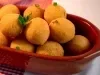 Fotografia de bolinhas de queijo dentor de um recipiente oval marrom de vidro sobre um pano vermelho quadriculado com branco, o qual está apoaido em uma mesa branca.