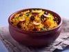 Tigela de porcelana redonda com porção de arroz amarelo e soltinho com amêndoas e uvas-passas pretas, decorado com folhas de cheiro-verde.