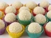 Fotografia de vários beijinhos passados no coco dentro de forminhas coloridas sobre uma mesa branca.
