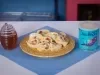 Fotografia em tons claros de um pano azul e quadrado sobre uma mesa de tom claro. Sobre esse paninho tem um prato desenhado amarelo, de vidro, com os sushis de frutas. Ao lado do prato tem a lata de ascenda e um vidro com mel.
