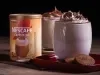 Foto da receita de cappuccino super cremoso servida em dois copos de vidro sobre uma louça vermelha em cima de uma mesa de madeira